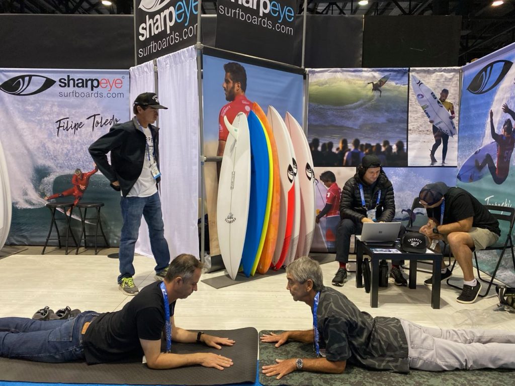 Gerry Lopez, right, practicing yoga on the show floor 